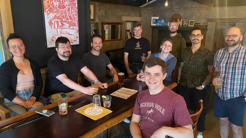 A group of 9 people around a table in a pub smiling at the camera